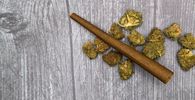 Several bright green medical marijuana buds on a wooden surface with a brown hemp wrap on top.