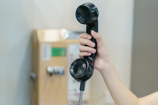 Woman hand holding a public phone, coin pay telephone on payphone tube or telephone booth.