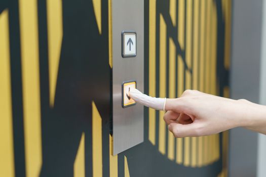 Woman wearing rubber for finger pressing a down button of elevator button inside the building. void direct contact during the outbreak of Covid-19.