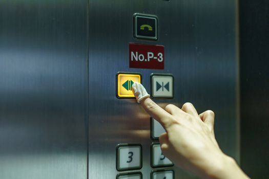 Woman wearing rubber for finger pressing a button of elevator button inside the building. void direct contact during the outbreak of Covid-19.
