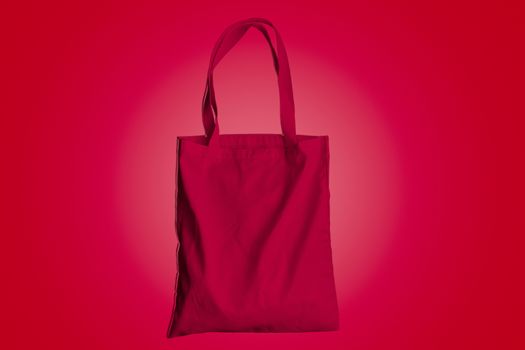 Reusable bag for groceries and shopping, red fabric tote bag on red background.