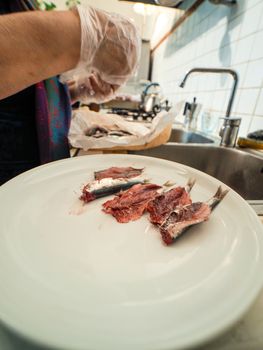 hands of senior housewive pensionate woman wearing transparent gloves cleaning anchovies fish from head and guts
