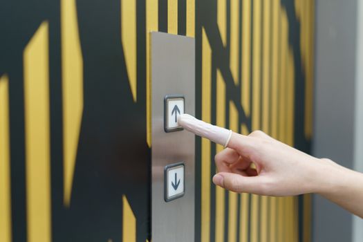 Woman wearing rubber for finger pressing a up button of elevator button inside the building. void direct contact during the outbreak of Covid-19.