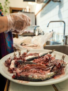 hands of senior housewive pensionate woman wearing transparent gloves cleaning anchovies fish from head and guts