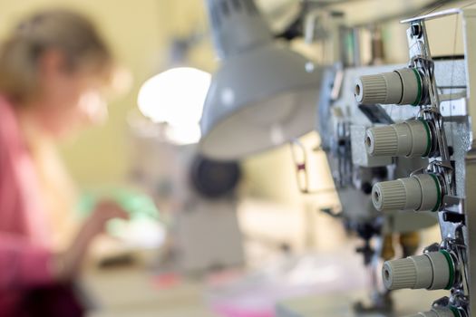 close-up of sewing equipment with threads and a worker in the background