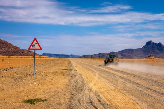 Namibrand Nature Reserve, Namibia - March 28, 2019 : Car passing a giraffes warning road sign on a gravel road in the desert of Namibia.