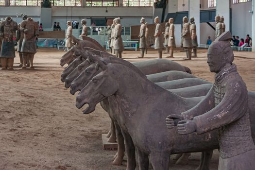 Xian, China - May 1, 2010: Terracotta Army museum and hall.  Gray-beige sculptures of line of horses and group of soldiers dispersed at excavation.