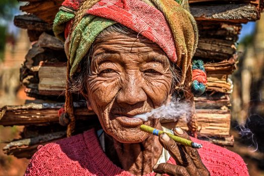 IN DEIN, MYANMAR - JANUARY 27, 2016 : old wrinkled woman smokes a cheroot cigar