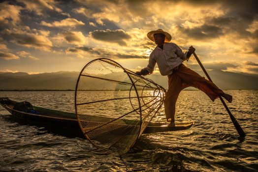 INLE LAKE, MYANMAR - JANUARY 28, 2016 : Burmese fisherman on a traditional bamboo boat catching fish using a handmade net at sunrise