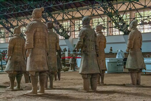 Xian, China - May 1, 2010: Terracotta Army excavation site. Group of Beige-gray statues of soldiers standing seen from back in large hall.