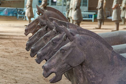 Xian, China - May 1, 2010: Terracotta Army excavation site. Group of gray statues of horses, focus on how heads form a row.