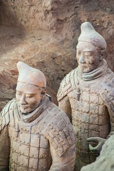 Xian, China - May 1, 2010: Terracotta Army excavation site. Closeup of 2 Beige-gray sculpture of soldiers standing in line behind each other in a trench.