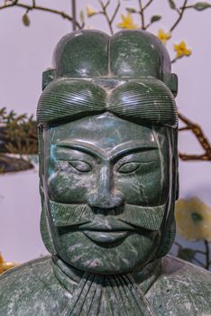 Xian, China - May 1, 2010: Terracotta Army museum. Closeup of green marble sculpture of officer face against light backdrop with images of plants and yellow flowers.