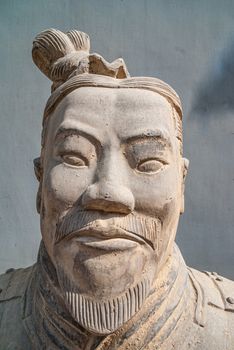 Xian, China - May 1, 2010: Terracotta Army museum. Face closeup of white-beige sculpture of older soldier against gray outside wall.