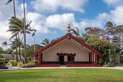 Laie, Oahu, Hawaii, USA. - January 09, 2020: Polynesian Cultural Center. Grand hall with maroon frames and warrior statue on top of the New Zealand Maori people under blue cloudscape. Green by foliage and lawn.