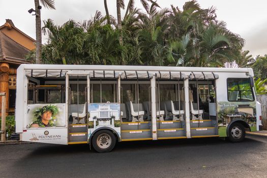 Laie, Oahu, Hawaii, USA. - January 09, 2020: Polynesian Cultural Center. White open public transport bus used inside the park with photo of young male polynesian man. Back is green palm trees.