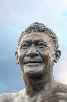 Laie, Oahu, Hawaii, USA. - January 09, 2020: Polynesian Cultural Center. Closeup of Bronze statue of face of Hamana Kalili against light blue cloudscape.