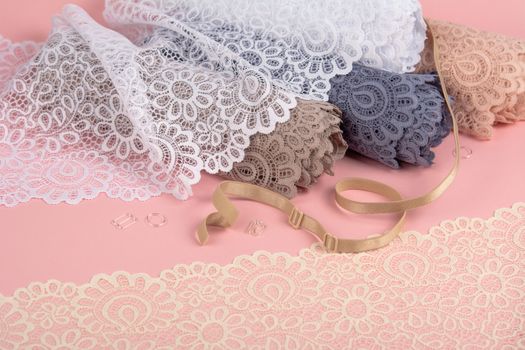 Roll of Delicate color laces for panties and bras on pink background with plastic fittings. Elastic material. Using for Atelier and fabric store.