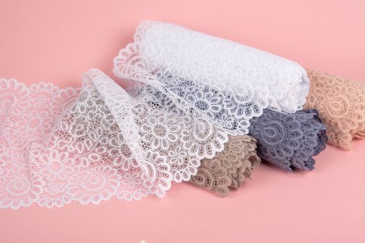 Roll of Delicate color laces for panties and bras on pink background with plastic fittings. Elastic material. Using for Atelier and fabric store.