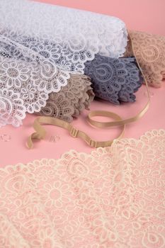 Roll of Delicate color laces for panties and bras on pink background with plastic fittings. Elastic material. Using for Atelier and fabric store.