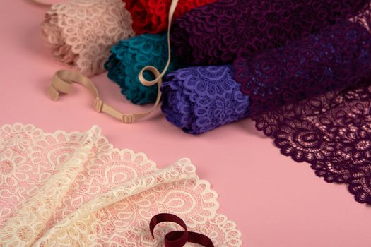 Roll of Delicate color laces for panties and bras on pink background with plastic fittings. Elastic material. Using for Atelier and fabric store.