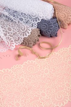 Roll of Delicate color laces for panties and bras on pink background with plastic fittings. Elastic material. Using for Atelier and fabric store.