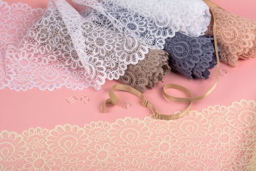 Roll of Delicate color laces for panties and bras on pink background with plastic fittings. Elastic material. Using for Atelier and fabric store.