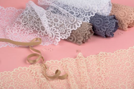 Roll of Delicate color laces for panties and bras on pink background with plastic fittings. Elastic material. Using for Atelier and fabric store.