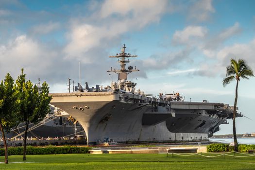 Oahu, Hawaii, USA. - January 10, 2020: Pearl Harbor. Gray Abraham Lincoln aircraft carrier docked under blue cloudscape with green foliage and lawn in front.