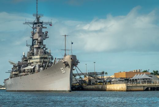 Oahu, Hawaii, USA. - January 10, 2020: Pearl Harbor. Bow of Gray USS Missouri docked and used as historic museum on blue water and under blue cloudscape. Brown buildings on shore.