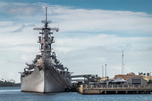 Oahu, Hawaii, USA. - January 10, 2020: Pearl Harbor. Bow of Gray USS Missouri docked and used as historic museum on blue water and under blue cloudscape. Brown buildings on shore.