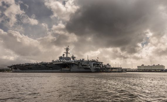 Oahu, Hawaii, USA. - January 10, 2020: Pearl Harbor. Long shot of Gray Abraham Lincoln aircraft carrier docked under full rain dark cloudscape on dark gray water.