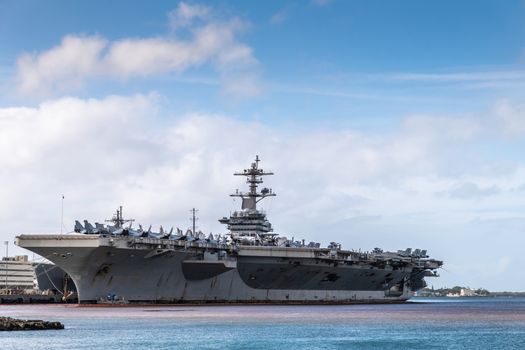 Oahu, Hawaii, USA. - January 10, 2020: Pearl Harbor. Gray Abraham Lincoln aircraft carrier docked under blue cloudscape and on blue and purple water.