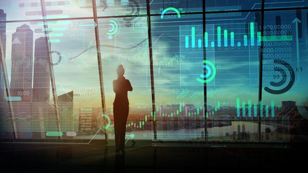 Silhouette of a business woman and a glowing array of data against the background of a panoramic window overlooking business center.