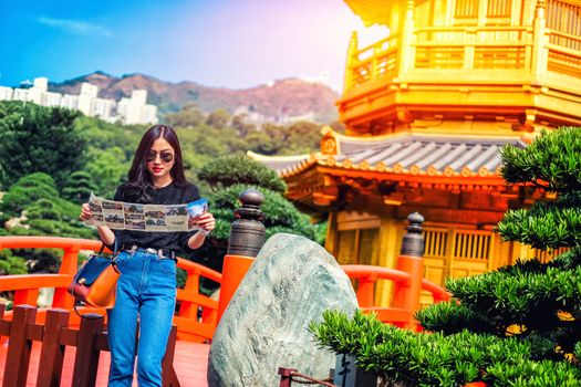 Young female tourist with map looking for a way to Gold Chinese pavilion Temple at the park in Hong Kong