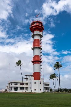 Oahu, Hawaii, USA. - January 10, 2020: Pearl Harbor Aviation Museum. Red and white control or watch tower of adjacent historic airfield under blue cloudscape. Green lawn and foliage.