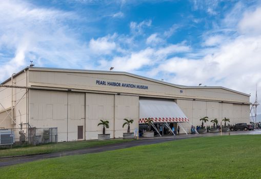 Oahu, Hawaii, USA. - January 10, 2020: Beige Pearl Harbor Aviation Museum hangar behind green lawn under blue cloudscape. People in line.