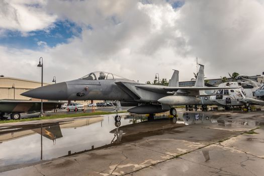 Oahu, Hawaii, USA. - January 10, 2020: Pearl Harbor Aviation Museum. Gray Fighter jet flown by Maj. Stuck Blake outside hangar under blue cloudscape and on wet tarmac.