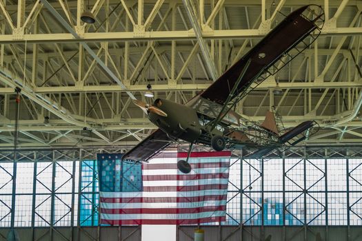 Oahu, Hawaii, USA. - January 10, 2020: Pearl Harbor Aviation Museum. small green airplane hangs from beige ceiling. Natural light through windows. Huge USA flag.