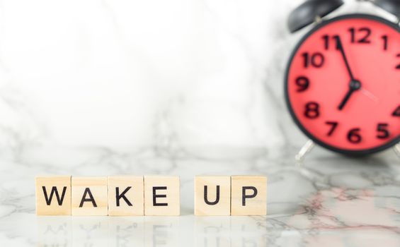 Wake up scrabble text on marble desk with alarm clock on the background with copy space