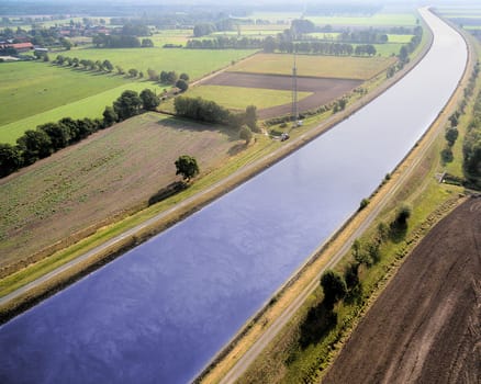 Canal from above, diagonally through a cultivated landscape with fields and meadows