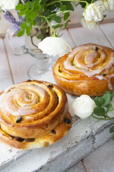 Freshly baked sweet bun with raisins on shabby white background with tender rose