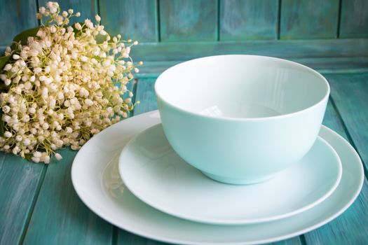 table setting with bouquet of lilies of the valley, empty dishes in teal color