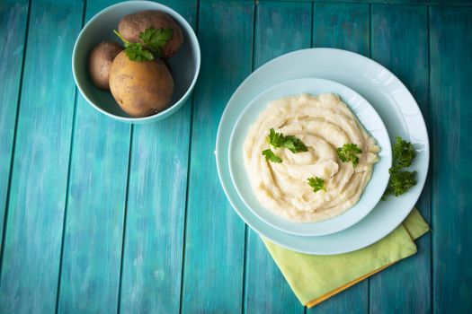 Delicious mashed potatoes with greens in bowl on blue teal wooden table top view