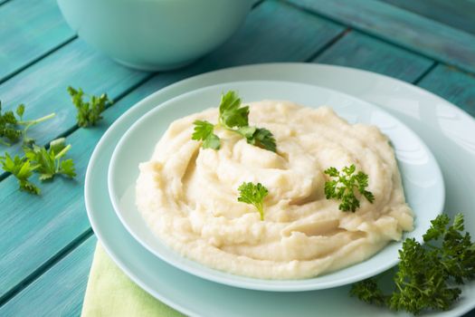 Mashed pureed potato in bowl on wooden table with persil