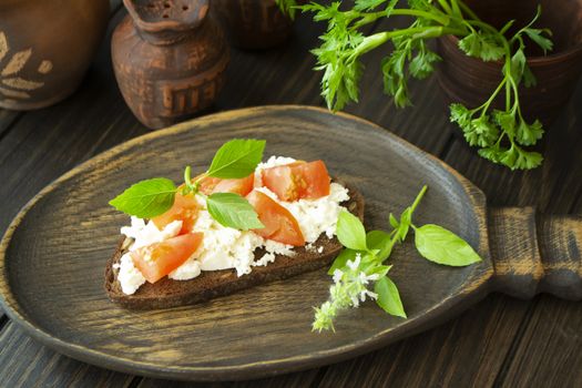 Bruschetta with fresh ricotta cheese, basil, red tomato on dark wooden board
