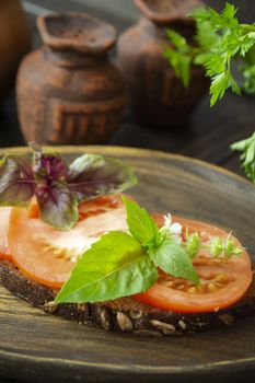 Dark bread bruschetta with red tomatoes and green basil leaves close up on a wooden textured rustic plate. Vertical image