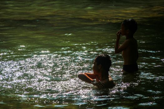 Two children are playing in the waterfall in a fun way.