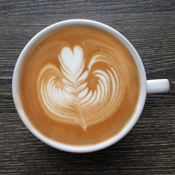 Top view of a mug of latte art coffee on timber background.