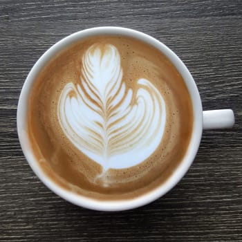 Top view of a mug of latte art coffee on timber background.